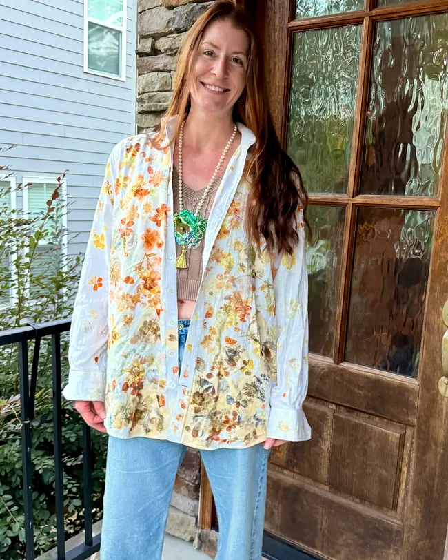Maker on a front porch in a white button-down shirt covered in orange and gold flower prints