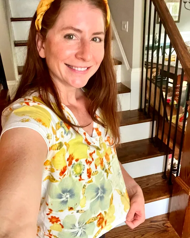Smiling maker in a white tee printed with yellow and orange botanicals, wearing a marigold-dyed yellow headband