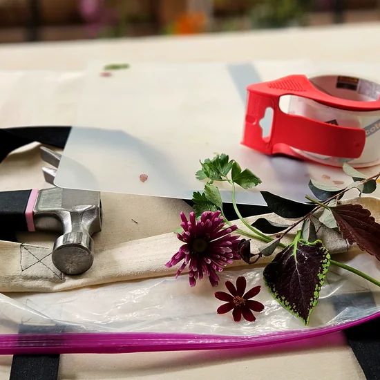 Module 2: home pounding station with hammer, clear cutting board, packing tape, ziplock bag, and fresh flowers on a tote