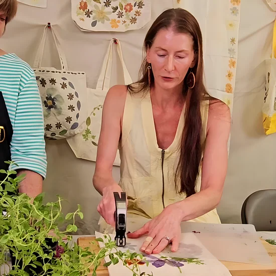 Module 4: Kristi hammering flowers into a tote bag on a cutting board while Theresa watches